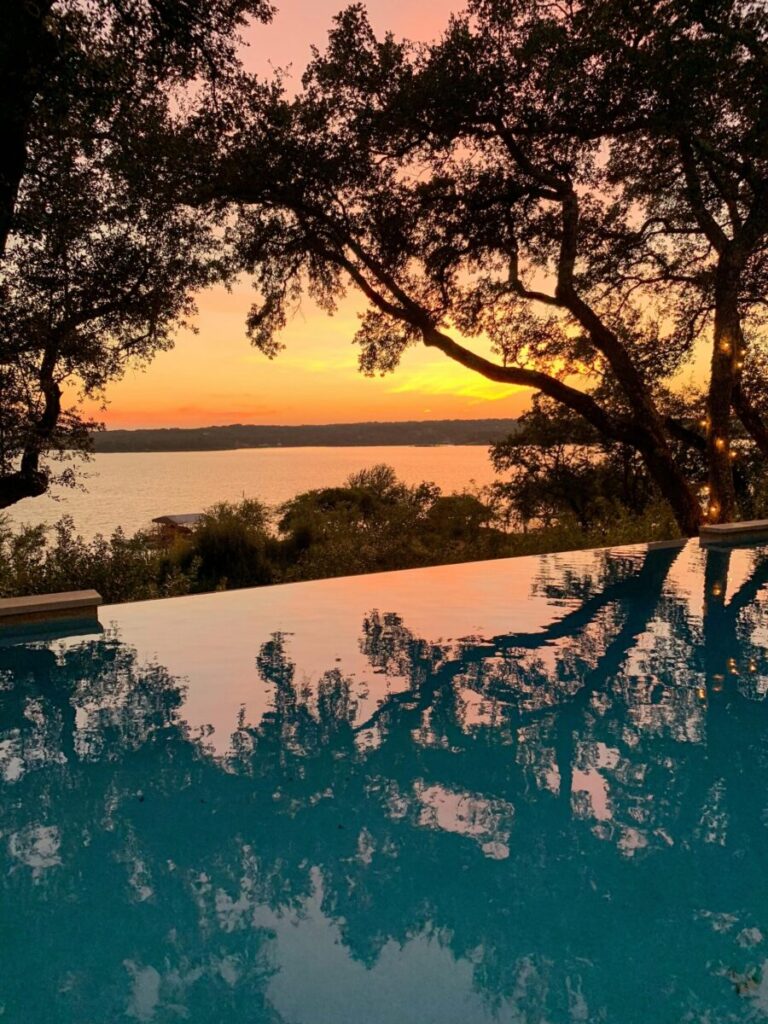 Capture the serene beauty of an Austin sunset reflecting over an infinity pool with vibrant colors.